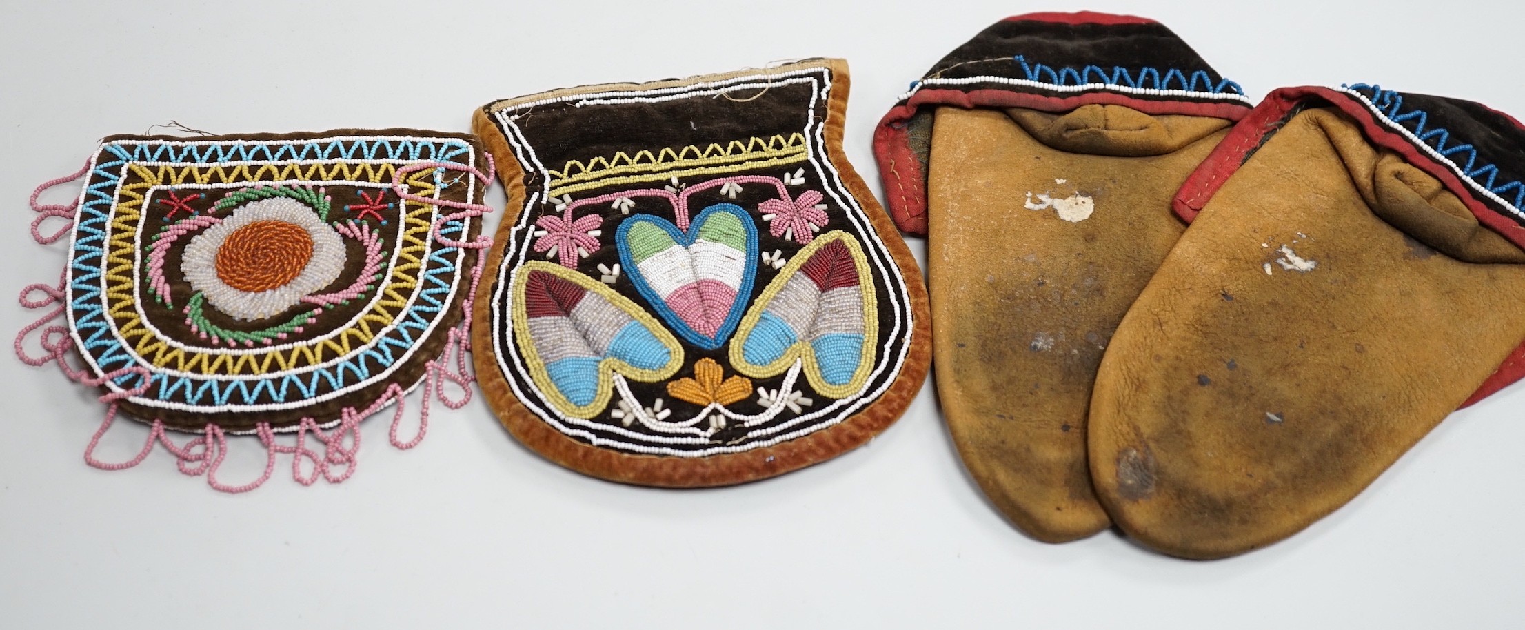 A pair of mid to late 19th century North American Indian moccasins, worked in floral beadwork on vamp, with velvet cuffs and red silk ties, together with two similar embroidered floral bead-worked bags on velvet